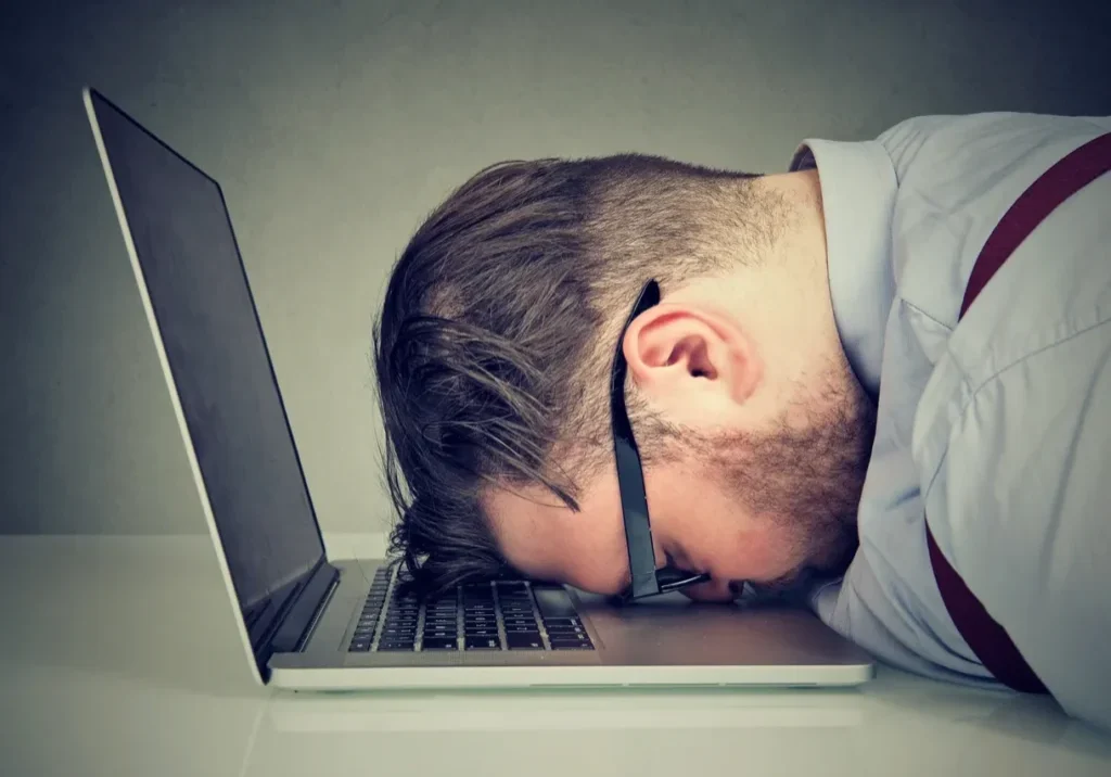 Man with head on laptop, looking exhausted.