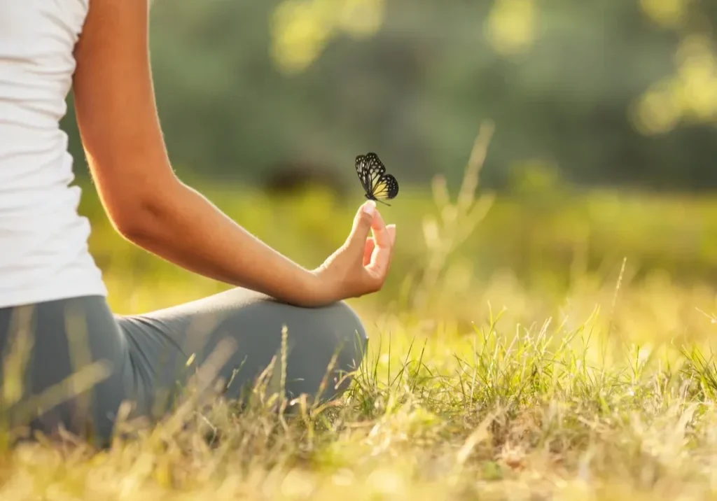 Person meditating outdoors with a butterfly.